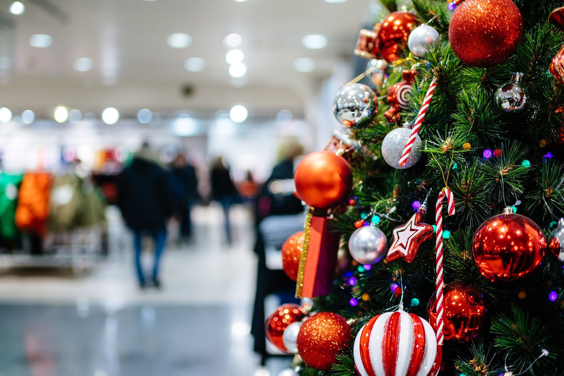 Christmas tree decorated with ornaments in a store. Shoppers are blurred in the background.