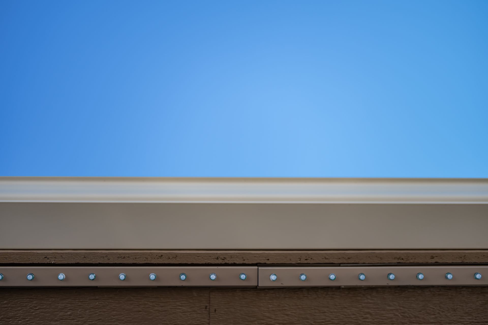 Blue sky above a rooftop edge with beige trim and brown siding accents