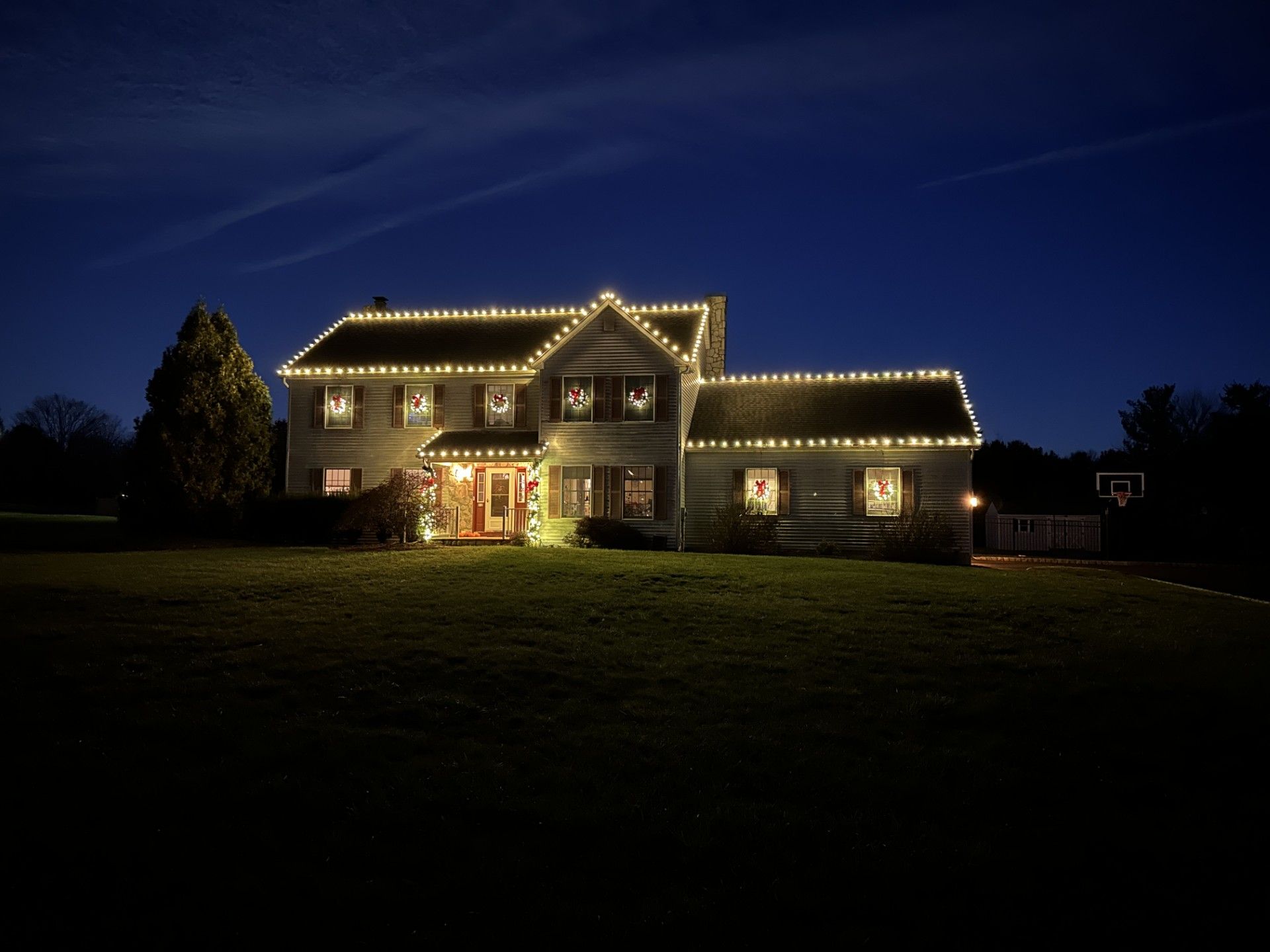 House at dusk with Christmas lights along the roofline and around the windows.