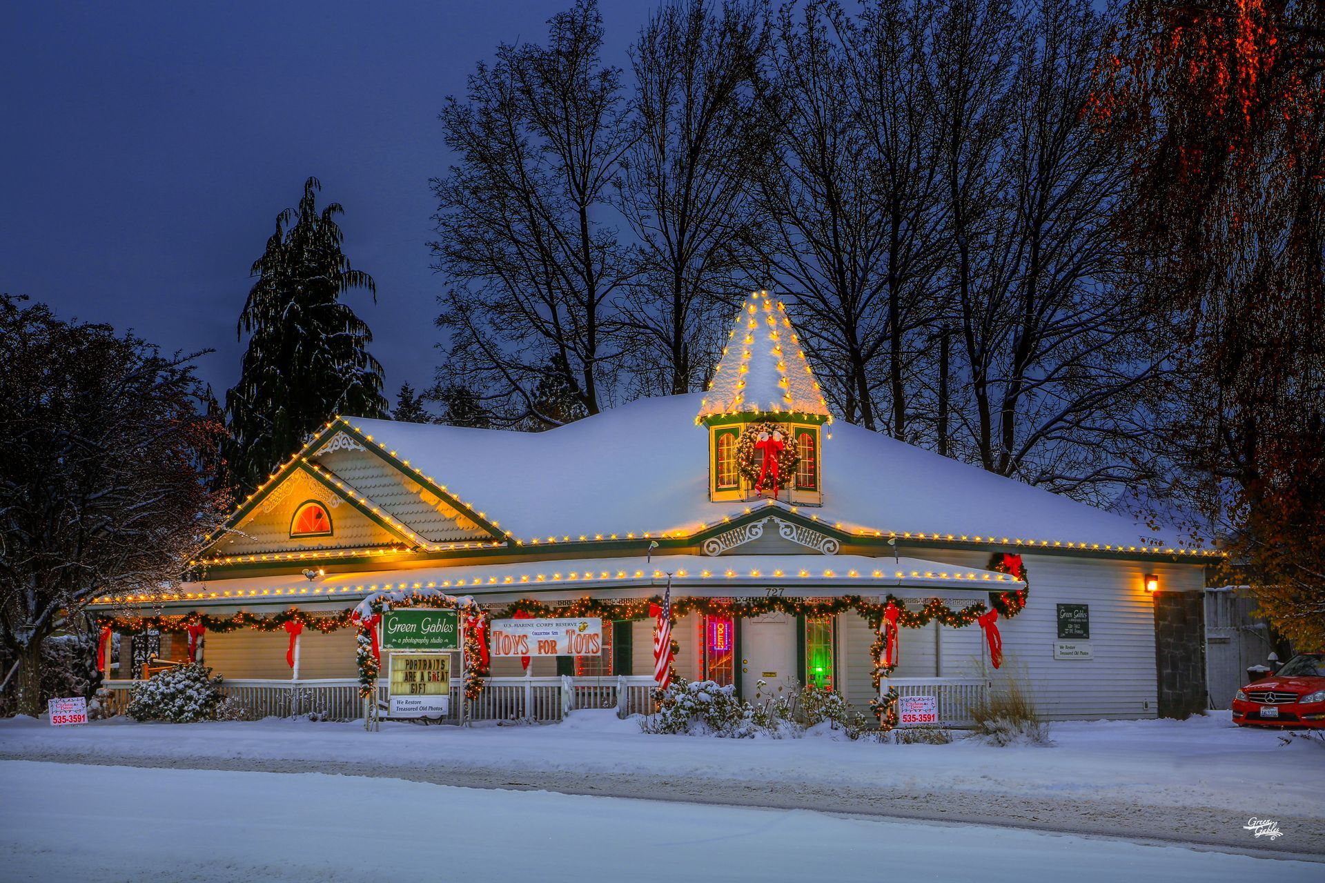 Snow-covered, decorated building with Christmas lights at dusk.