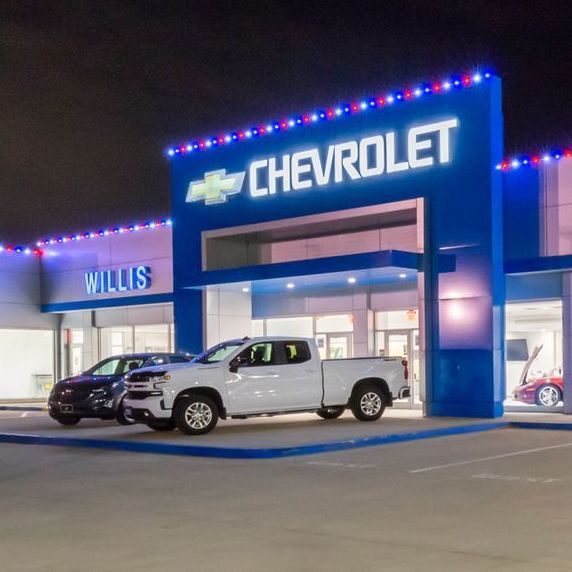 Chevrolet dealership at night, vehicles parked out front. Blue and red lights accent the building.
