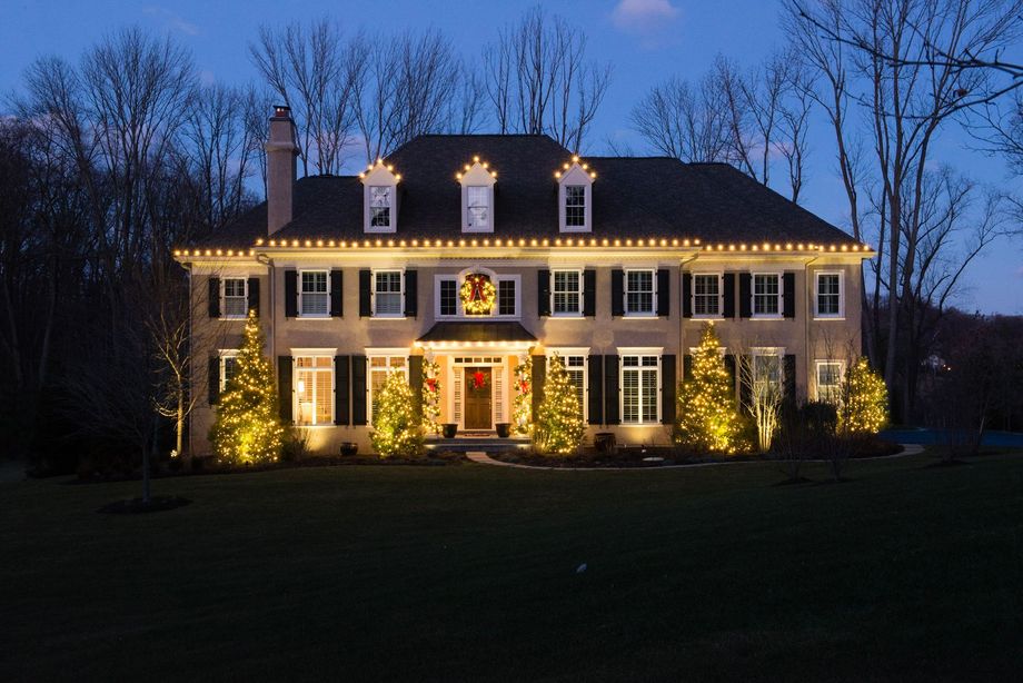 Large house at night, decorated with Christmas lights on the roof and trees.