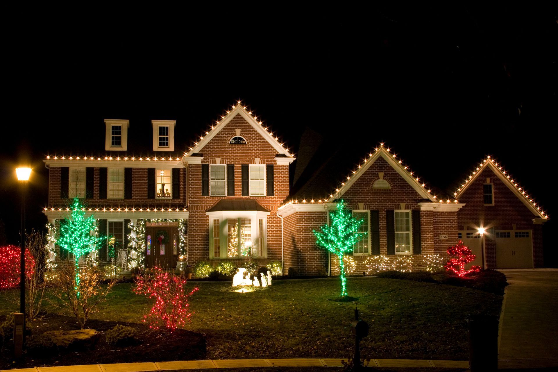 House decorated with Christmas lights; red and green lights illuminate trees and rooflines.
