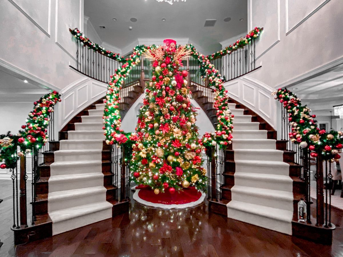 Grand foyer decorated for Christmas with a large tree, garland, and dual staircases.