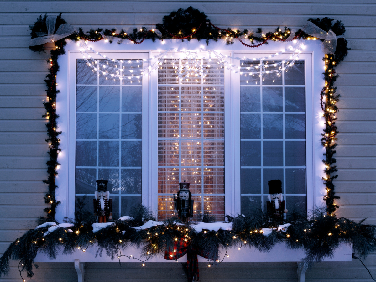 Window with Christmas lights and decorations; three nutcrackers on the windowsill.