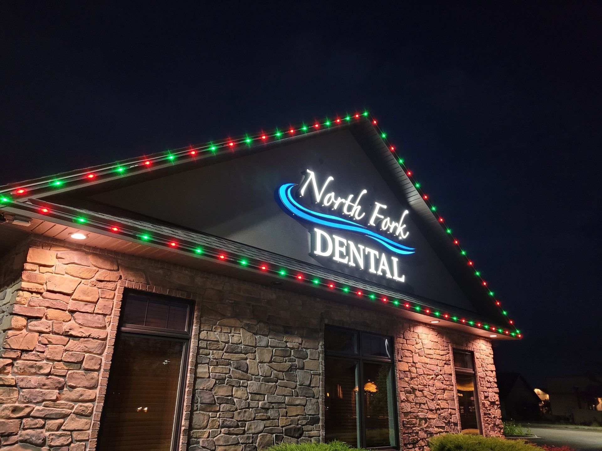 North Fork Dental building with red and green Christmas lights along the roofline at night.