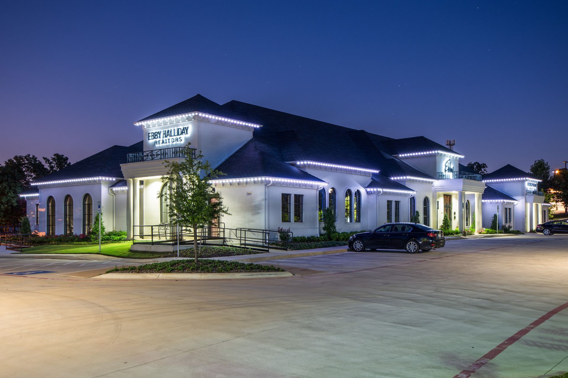 A large white building with a car parked in front of it at night.