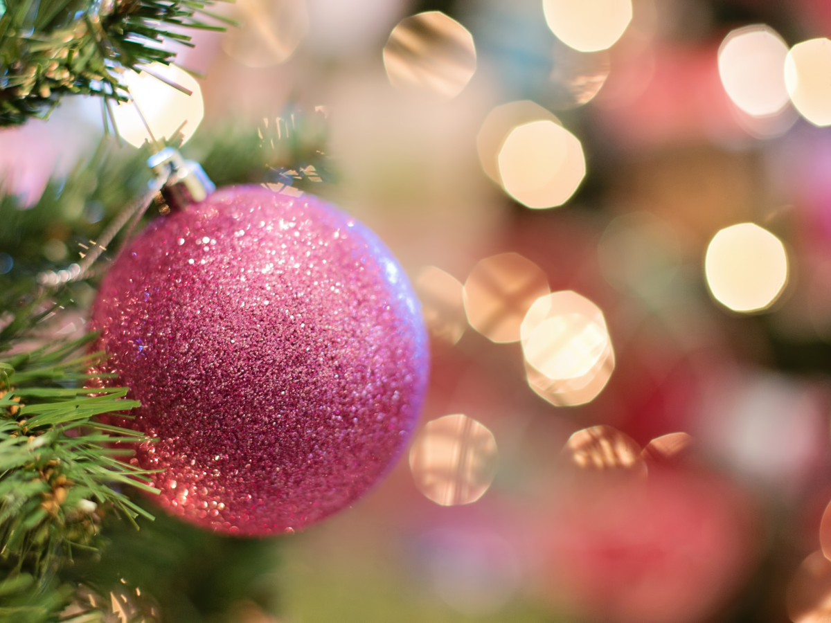 Pink glittery Christmas ornament on a tree, blurred warm lights in the background.