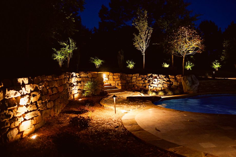 Stone wall with pathway and pool illuminated at night by landscape lighting.