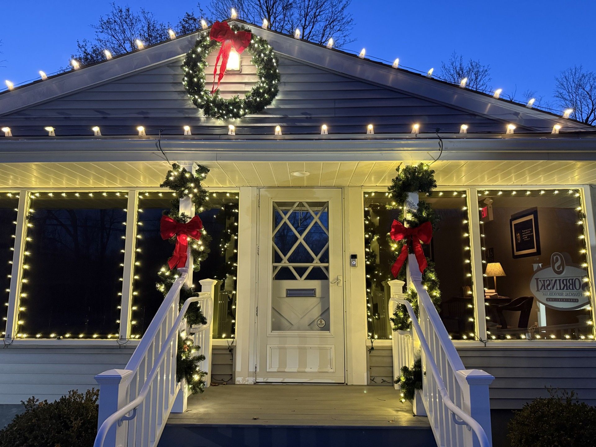 House decorated for Christmas with lights, wreaths, and red bows.