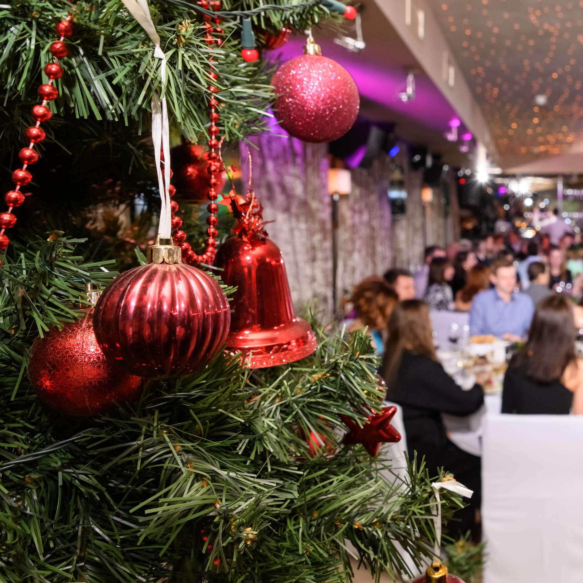 Christmas tree decorated with red ornaments in a restaurant, people are seated at tables in the background.