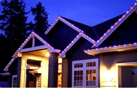 House decorated with red and blue Christmas lights along roofline at dusk.