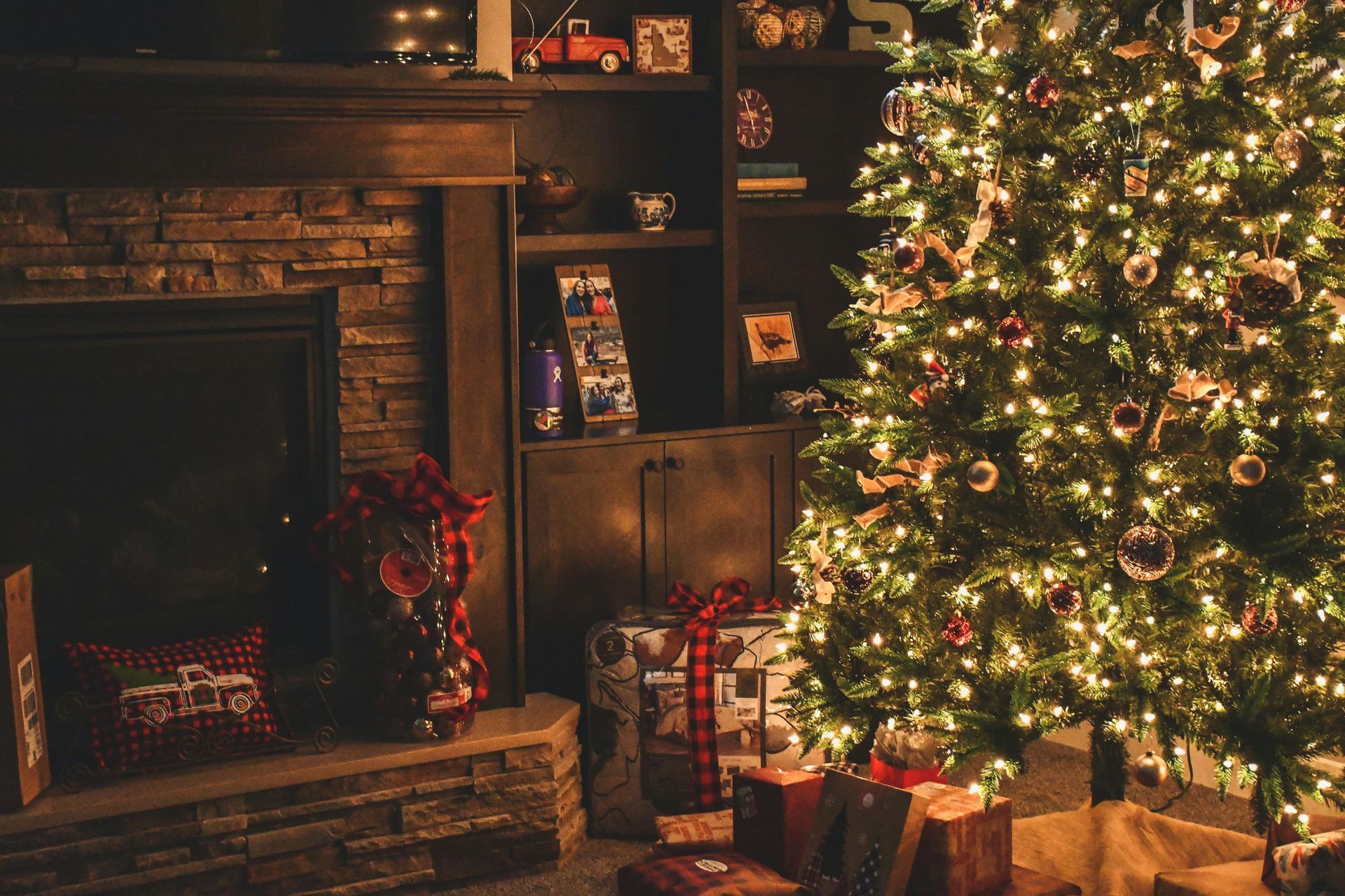 Christmas tree with glowing lights and wrapped presents near a fireplace.