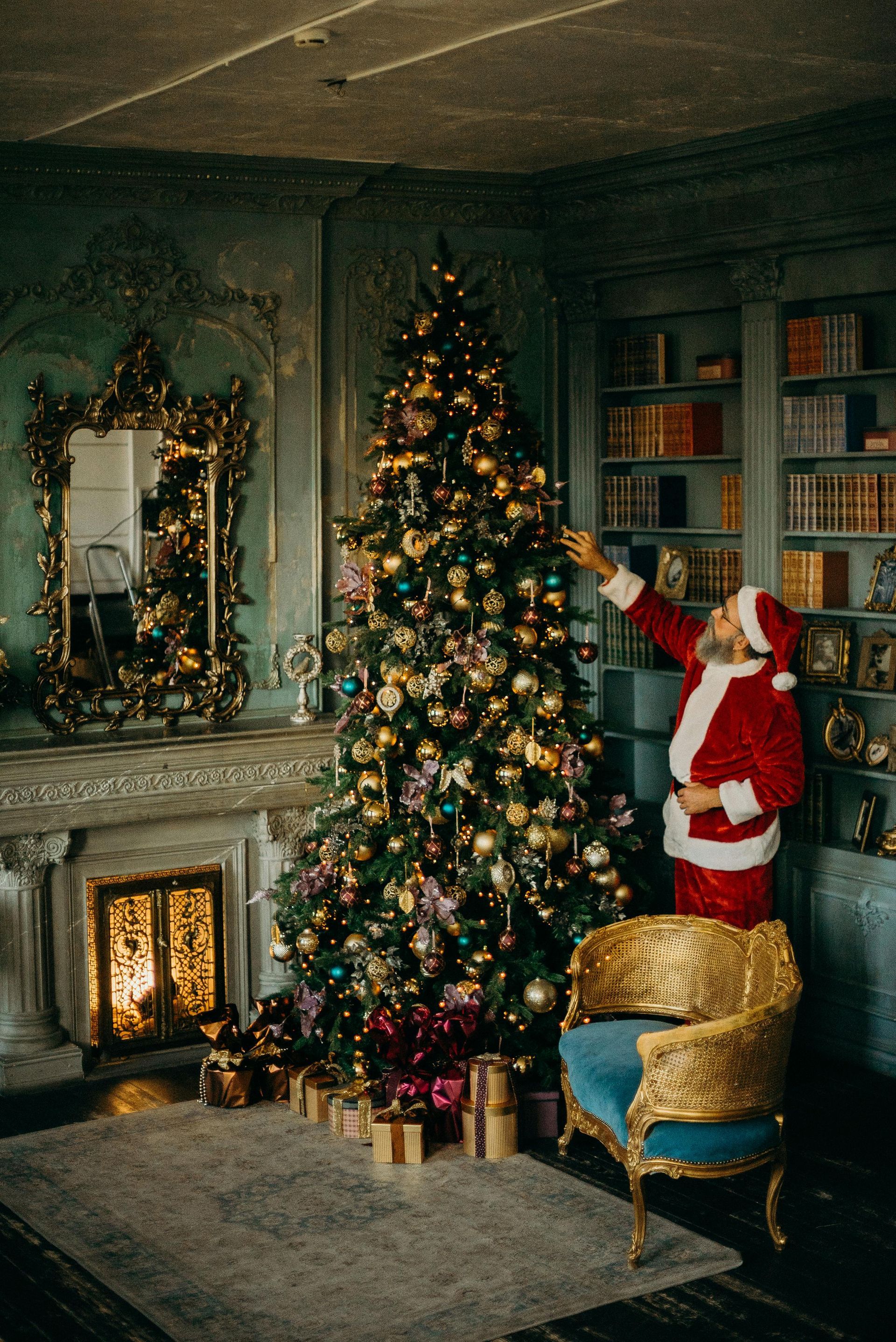 Santa claus is decorating a christmas tree in a living room.