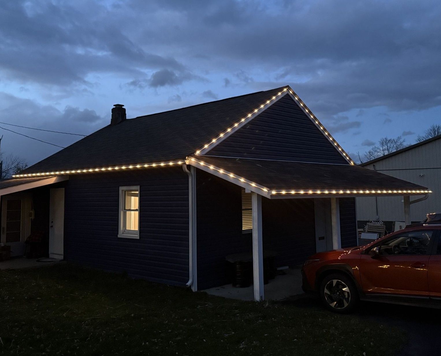 A house with christmas lights on the roof and a car parked in front of it.