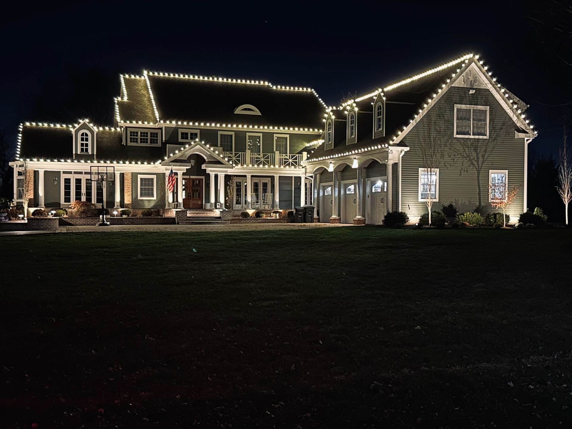 Large, multi-story house lit with white Christmas lights at night.