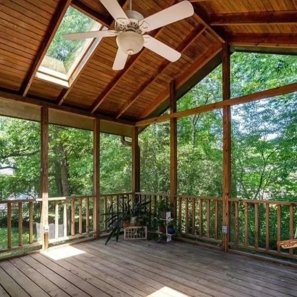 Wooden screened porch with a ceiling fan, overlooking a lush green yard and trees.
