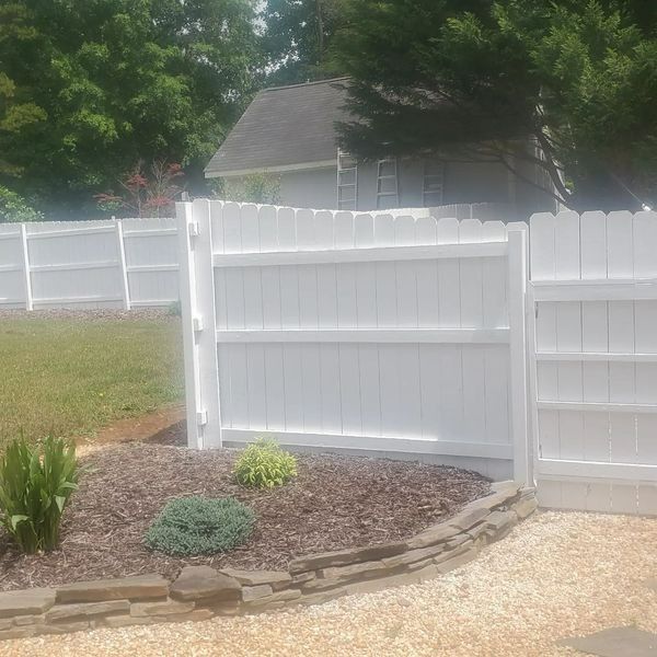 White picket fence with an open gate, grass, and landscaping.