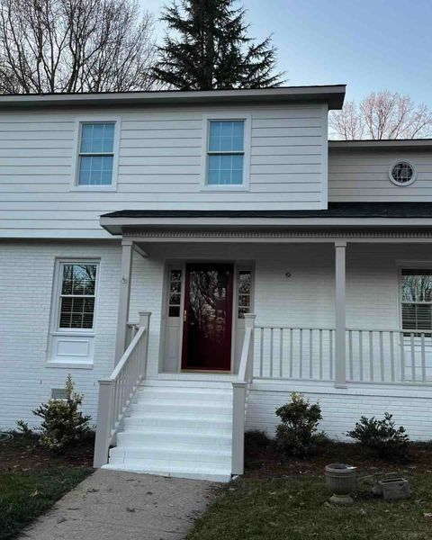 White two-story house with a red door, porch, steps, and blue windows.
