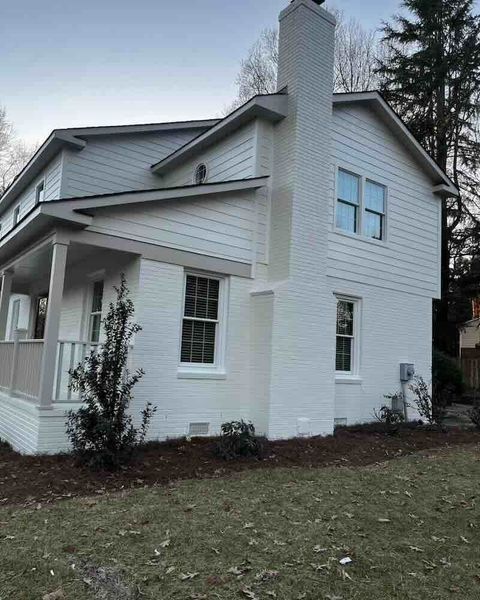 Two-story house with white brick exterior, chimney, and windows.