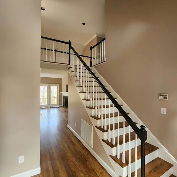 A staircase with white balusters and brown steps leading to a second-floor landing and open doorway, beige walls.