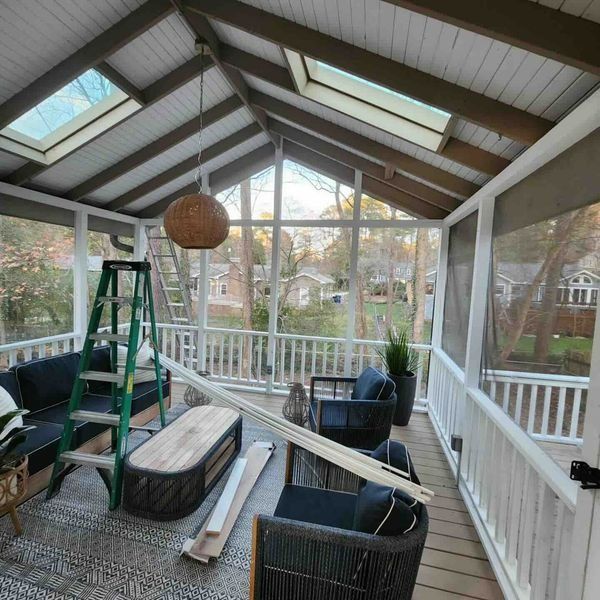 Screened porch with dark furniture, rug, skylights, ladder, and a wooden coffee table.
