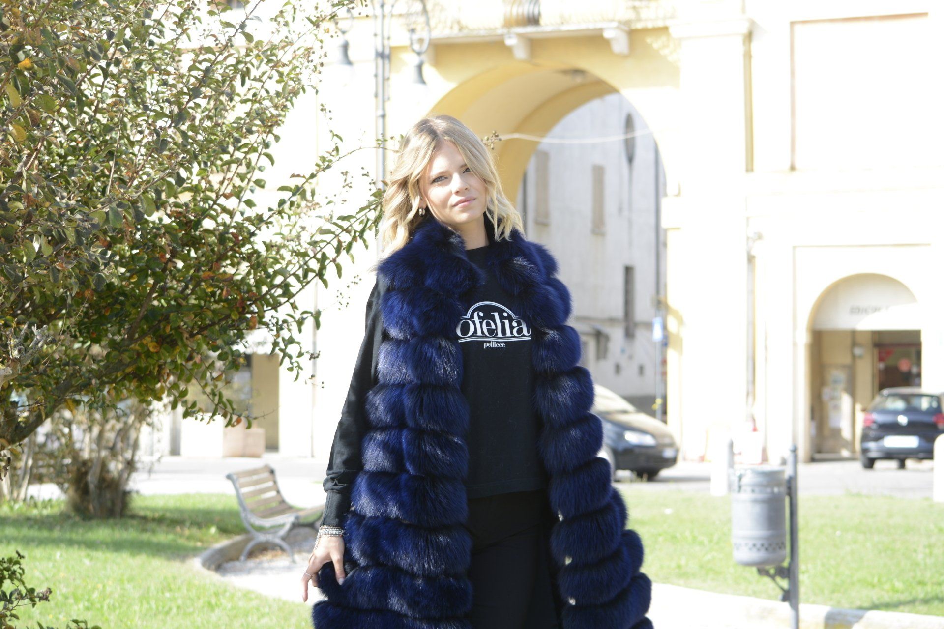 Donna che indossa un lungo gilet di pelliccia blu, in piedi davanti a un arco.