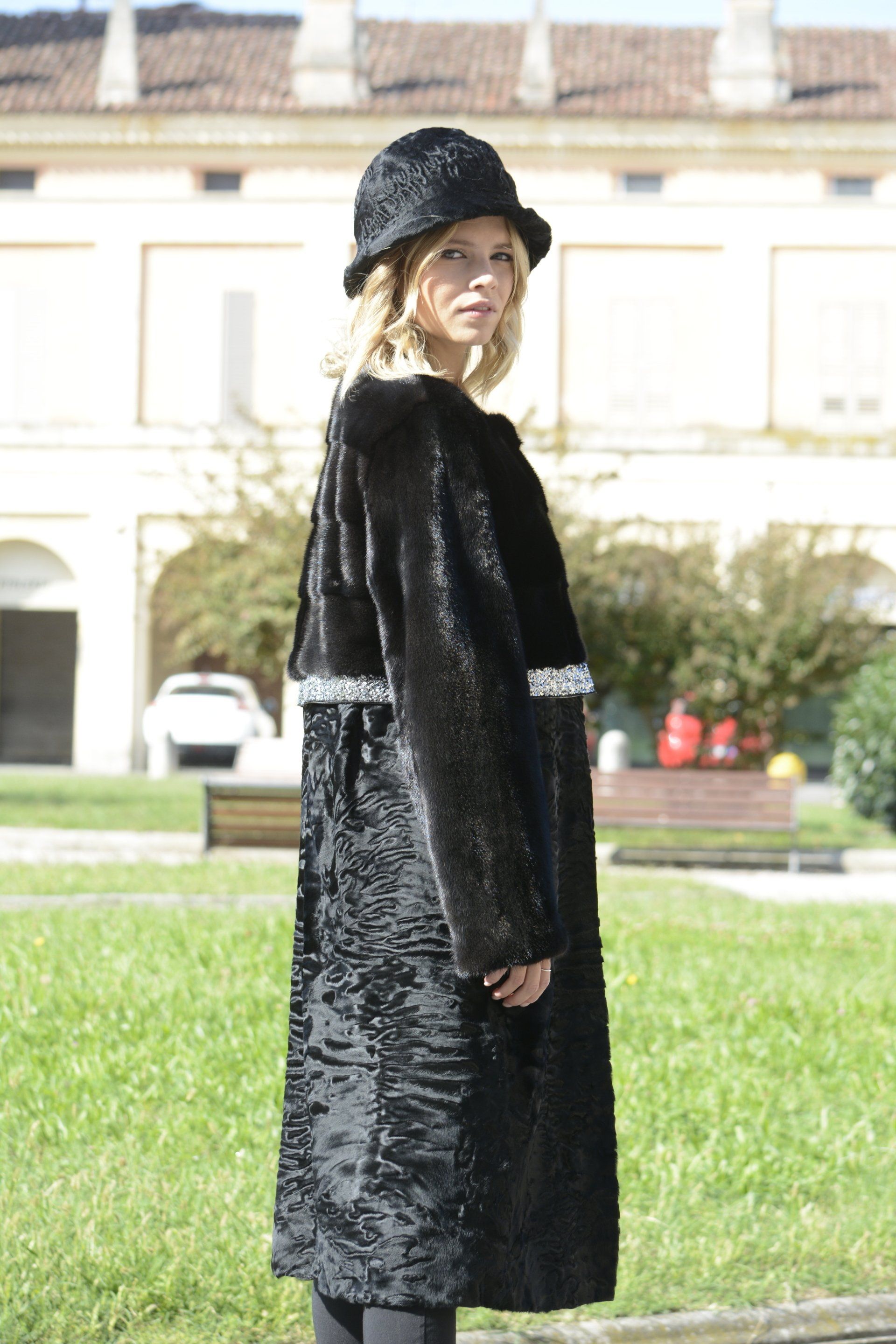 Una donna con pelliccia nera e cappello posa fuori da un edificio.