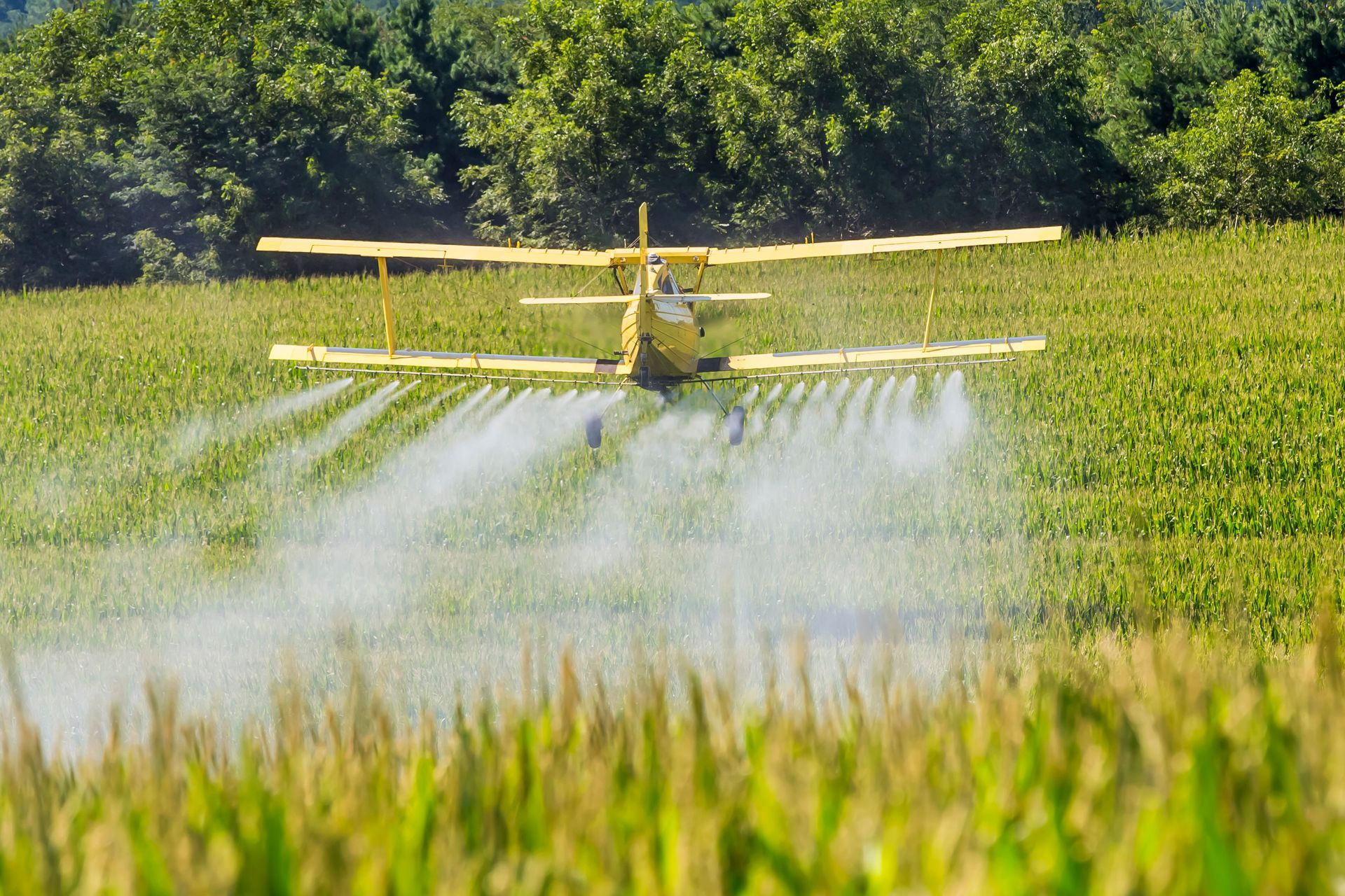 A yellow plane is parked on a runway with another plane flying in the background