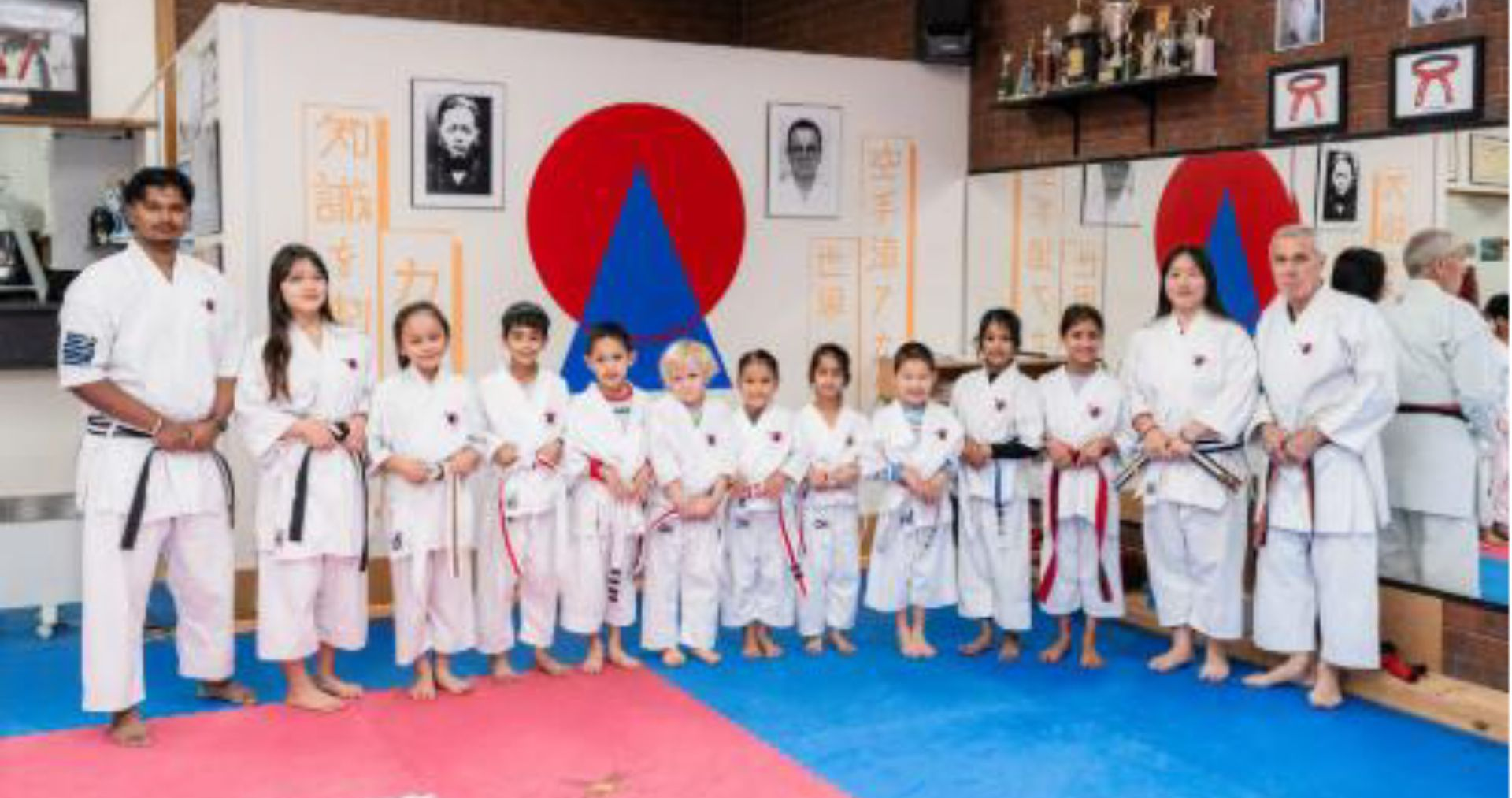 Group of karate students and instructors posing together in a dojo wearing white uniforms and belts. Group of karate students and instructors posing together in a dojo wearing white uniforms and belts.
