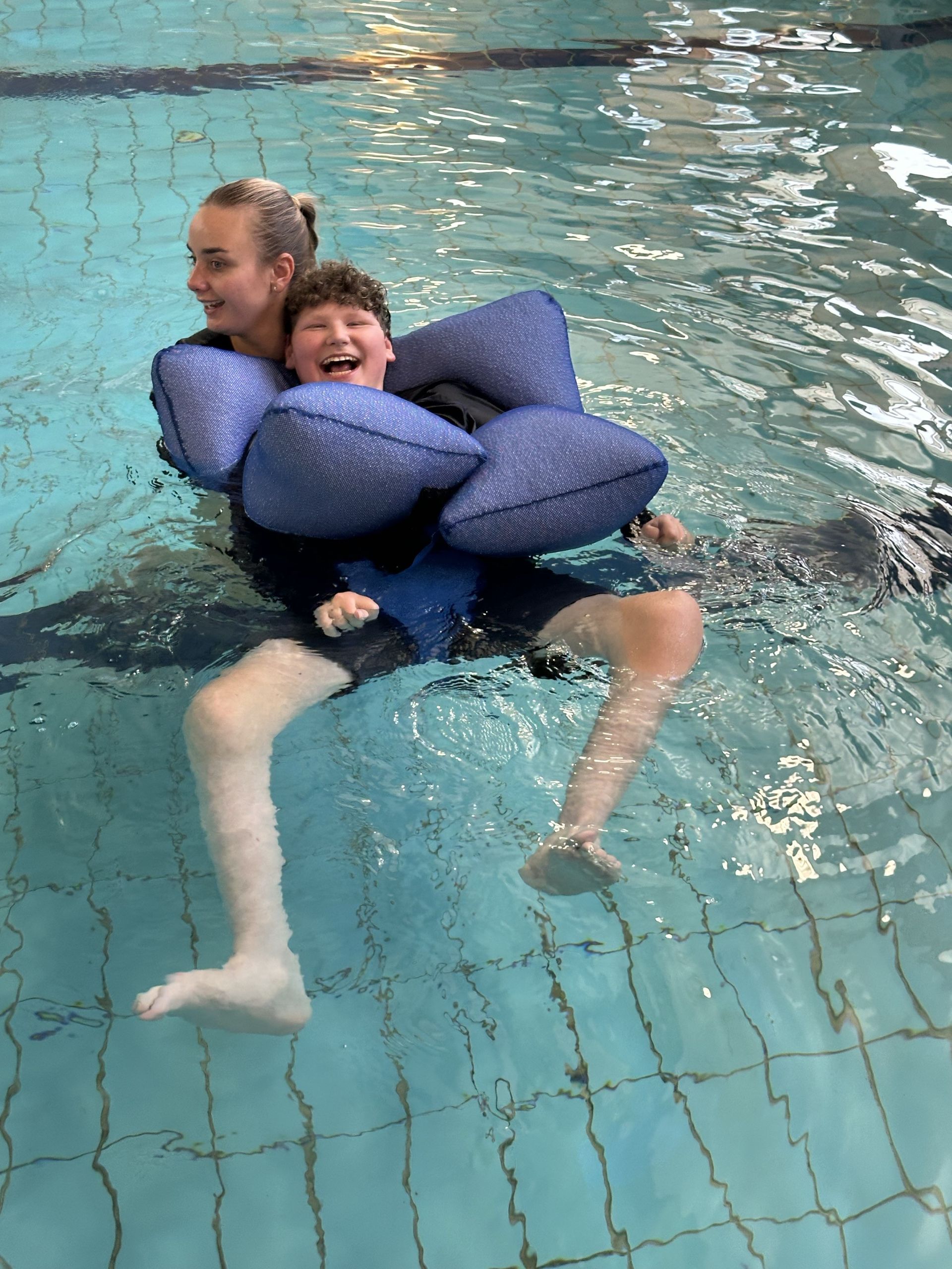 A boy and a woman are swimming in a swimming pool.