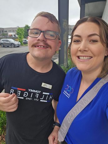 A man with glasses and a mustache is standing next to a woman in a blue shirt.