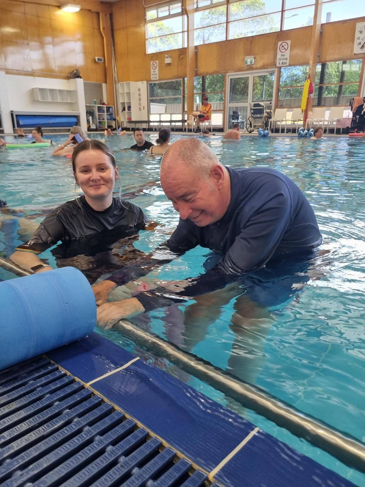 A boy and a woman are swimming in a swimming pool.