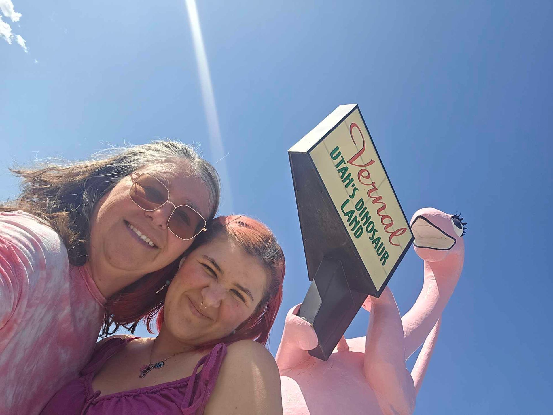 Two women standing next to a sign that says Vernal at Dinah the dinaosaur