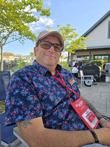 A man wearing a hat and sunglasses is sitting in a chair.