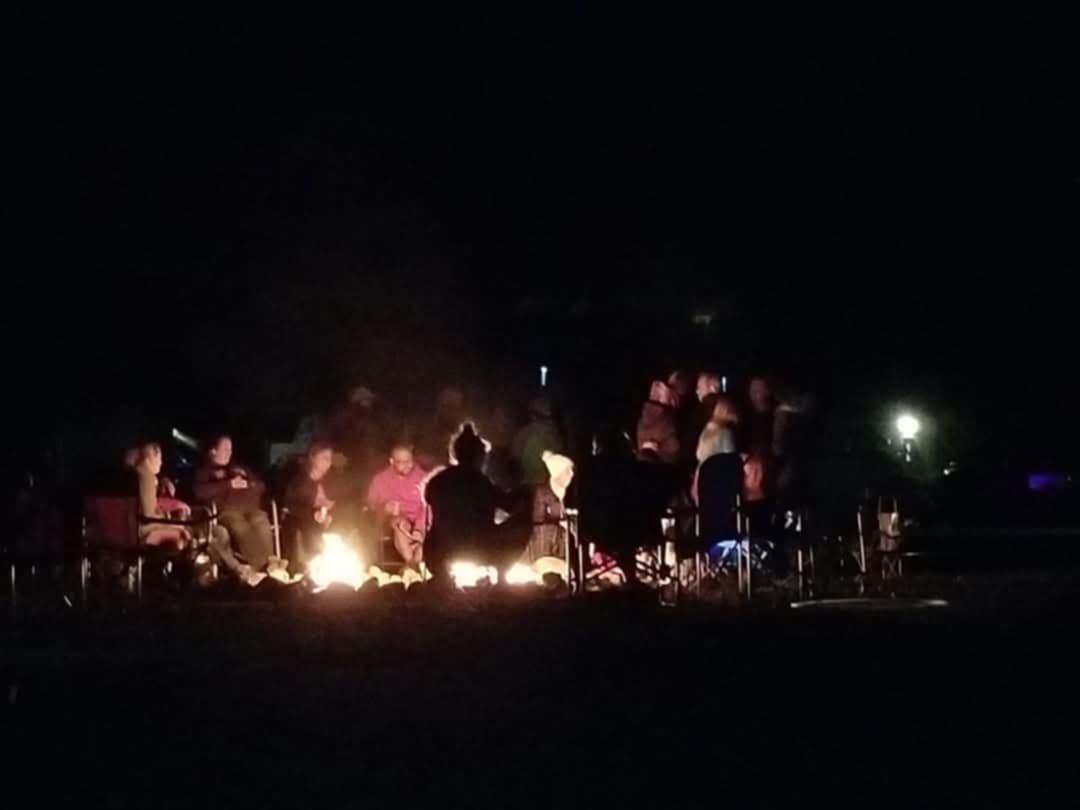 A group of people are sitting around a campfire at night.