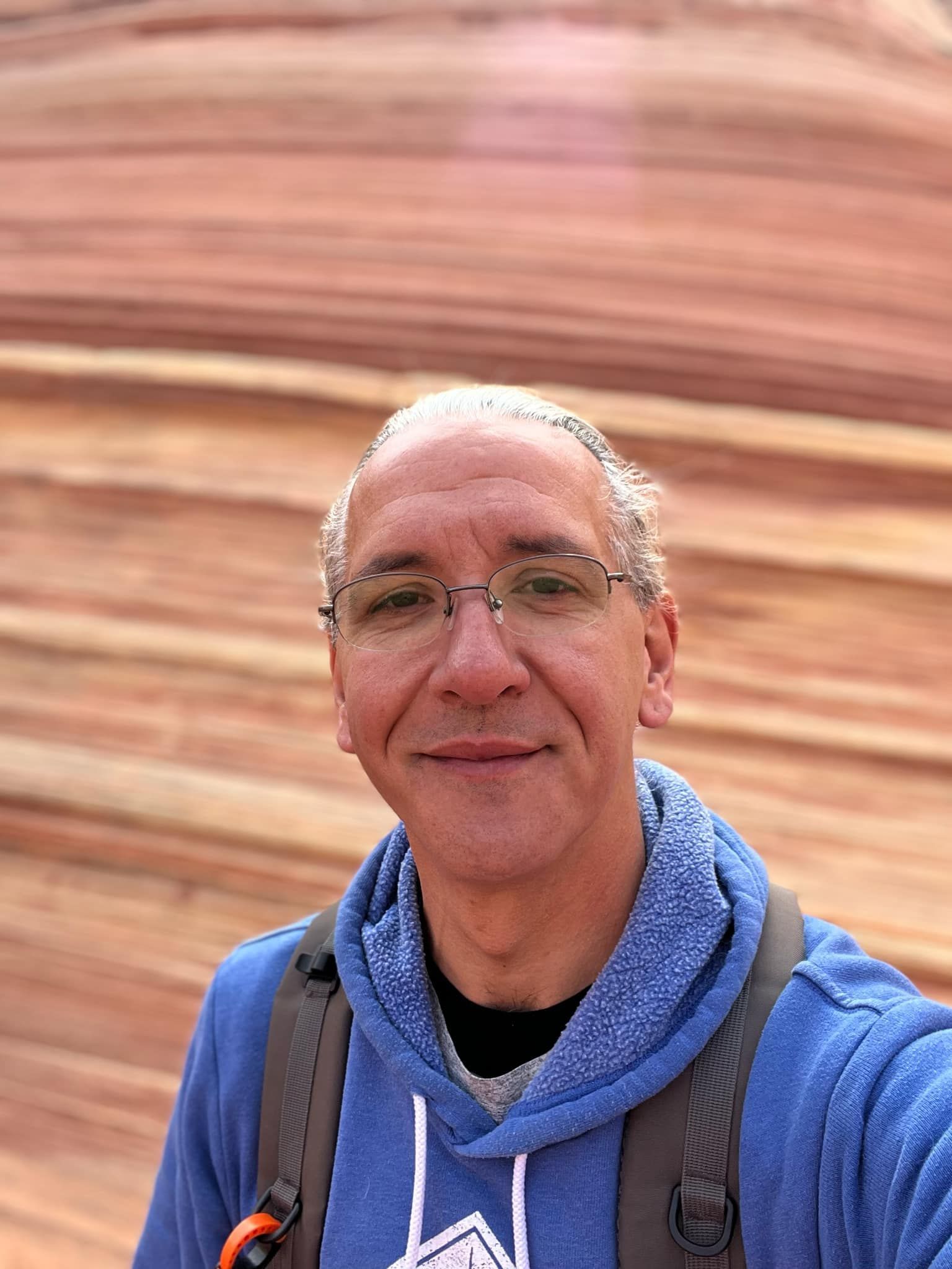 A man wearing glasses and a blue hoodie is taking a selfie.