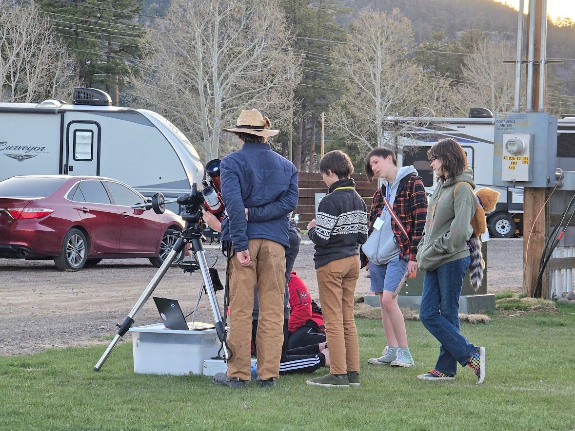 A group of people are standing in a field looking through a telescope.