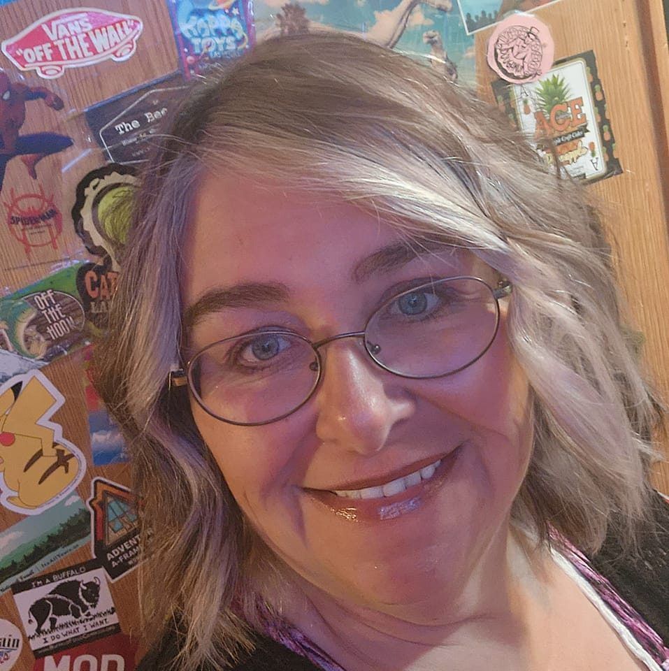 A woman wearing glasses is smiling in front of a wall covered in stickers.