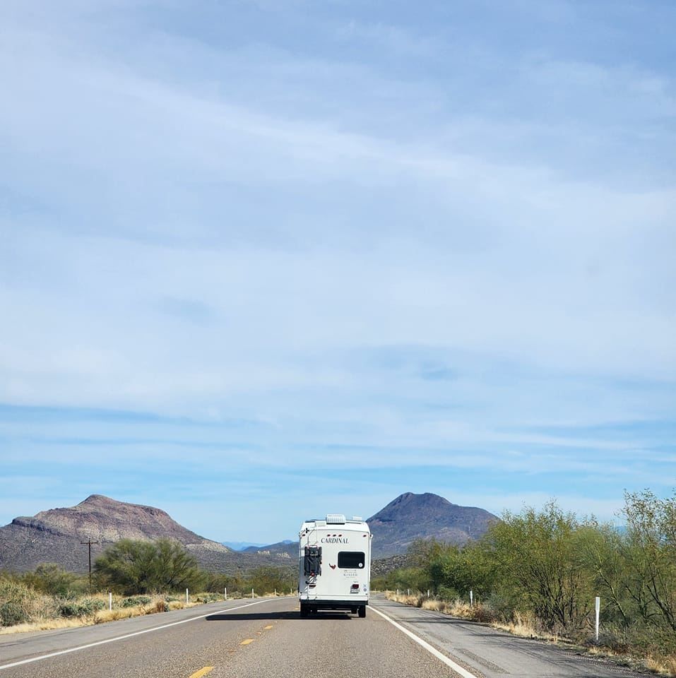 A white rv is driving down a desert road