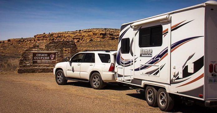 A white suv is towing a trailer in the desert.