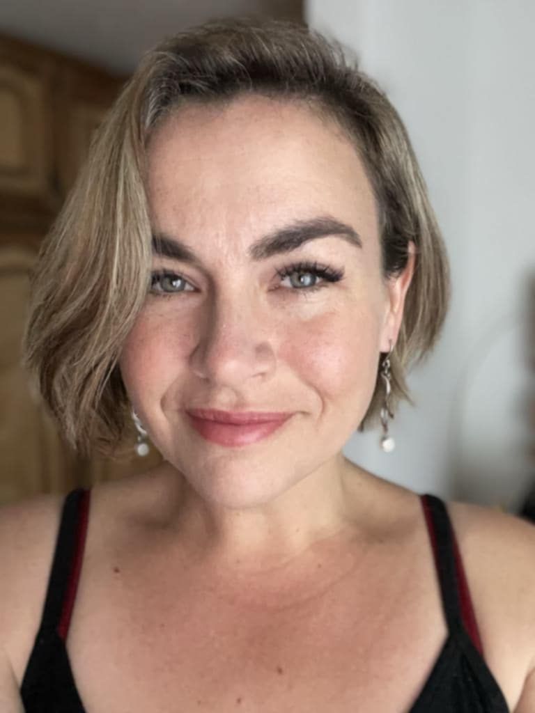 A woman wearing a black tank top and earrings is smiling for the camera.