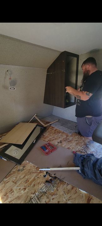 Man installing a cabinet in a room with damaged flooring.