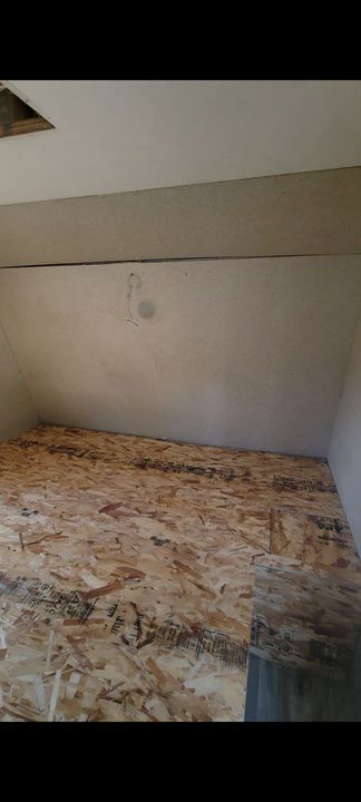 A small unfinished interior space with wood flooring and pale walls. A section of the ceiling has a hole.