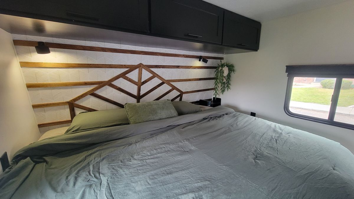 Bedroom in an RV with a bed, wooden headboard, and cabinets. Green bedding.
