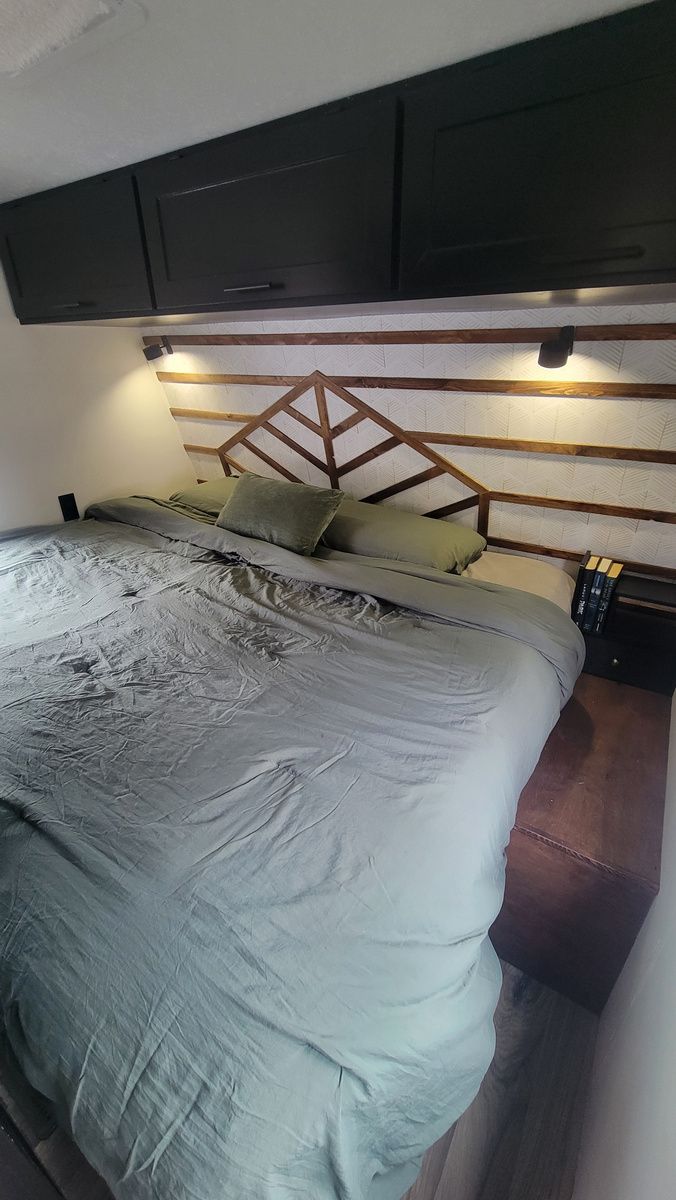Bedroom with a bed, wooden headboard, overhead cabinets, and a nightstand.