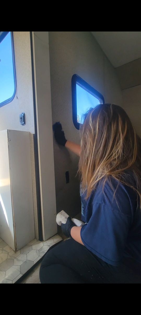 A person wearing black gloves cleans the interior of a vehicle with windows.