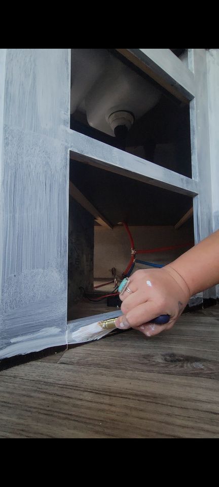 A hand painting a cabinet white. Wood floor visible. Inside of cabinet exposed.