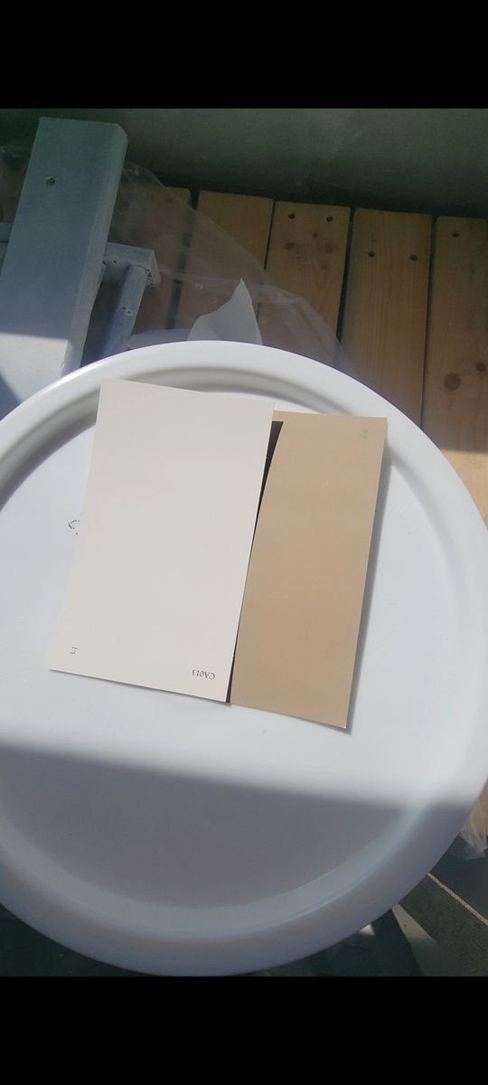 Two color swatches, one cream and one tan, on a white lid, with wooden planks in the background.