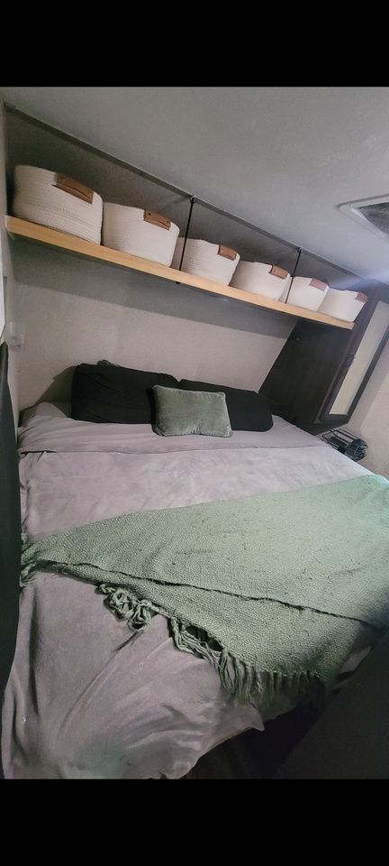 Bed in a camper with overhead storage and decorative throw.